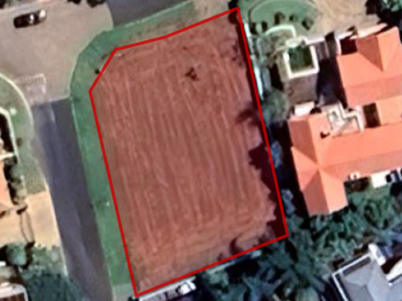 An aerial view of a vacant residential plot of land, clearly outlined in red, situated within a developed neighborhood.