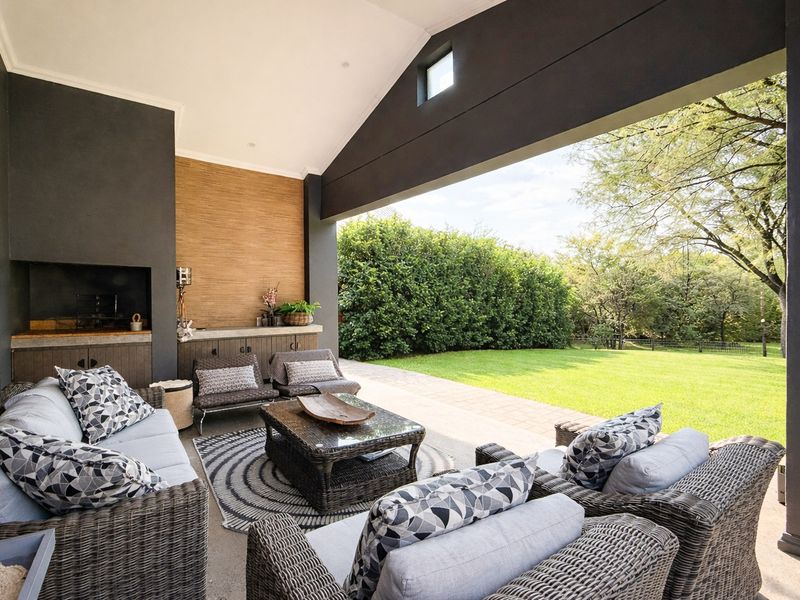 A spacious covered patio featuring a built-in braai, stone countertop, and vaulted ceiling, overlooking a well-maintained garden.