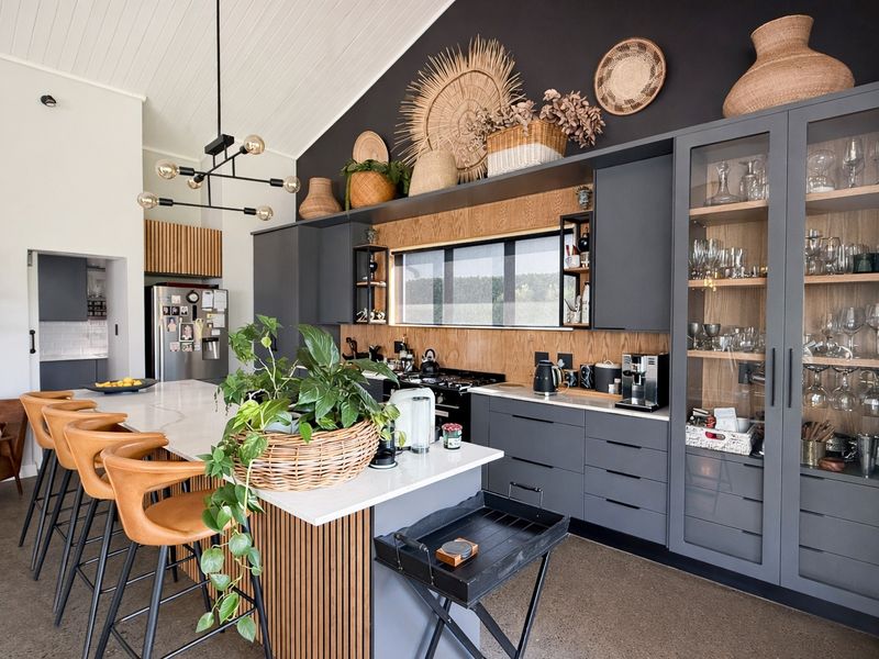 Modern kitchen featuring dark cabinetry, timber accents, a large central island with quartz countertops, and high-end built-in storage under a vaulted ceiling.