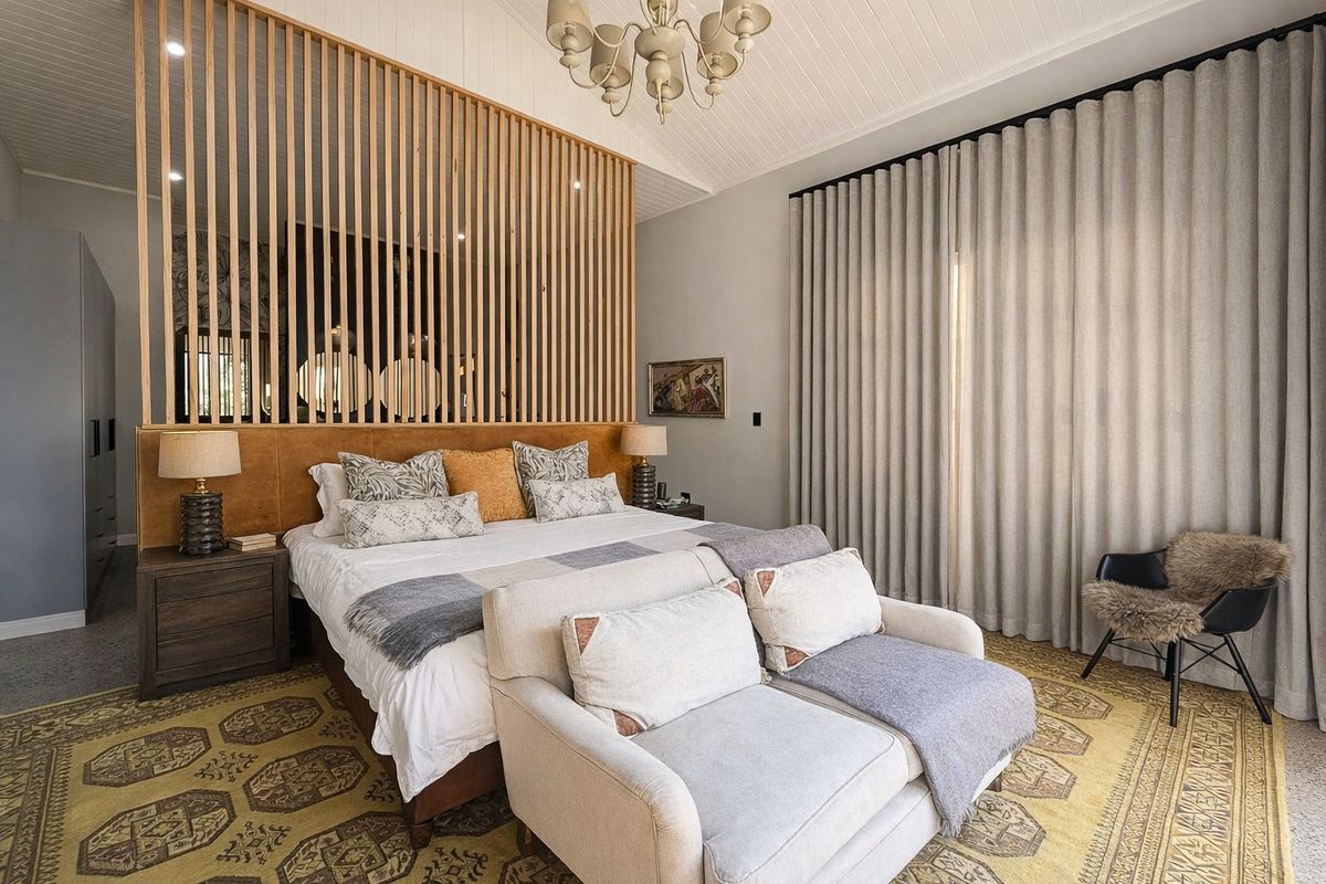 A well-appointed bedroom featuring a vaulted tongue and groove ceiling, a decorative timber slat room divider, and full-height window treatments.