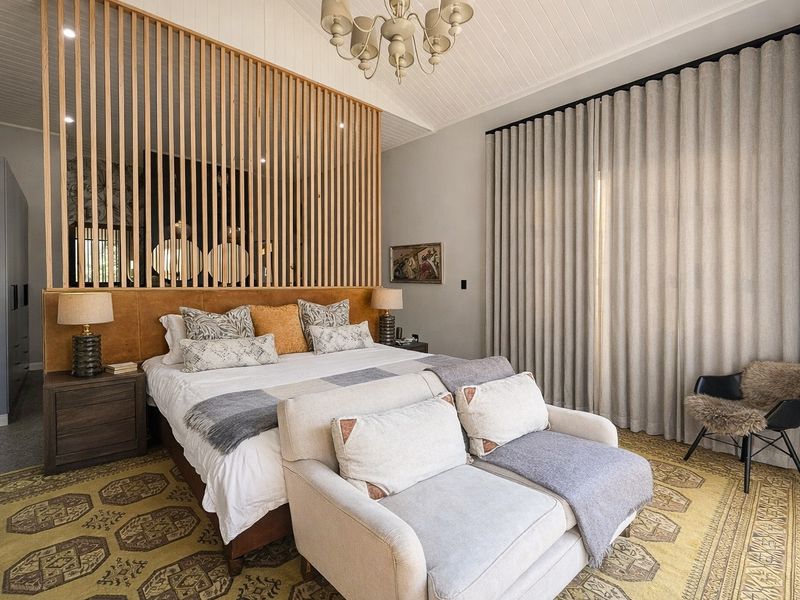 A well-appointed bedroom featuring a vaulted tongue and groove ceiling, a decorative timber slat room divider, and full-height window treatments.