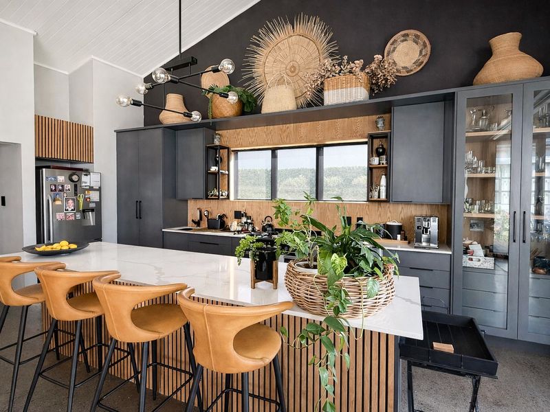 Modern kitchen featuring a large stone-topped island with slatted wood detailing, dark cabinetry, and a vaulted ceiling with contemporary lighting.