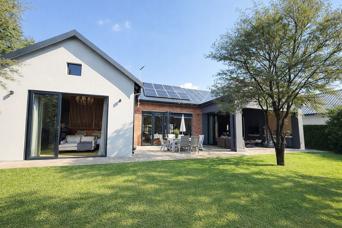 A well-maintained rear exterior view featuring a paved patio, bi-fold doors, and solar panels, overlooking a landscaped garden.