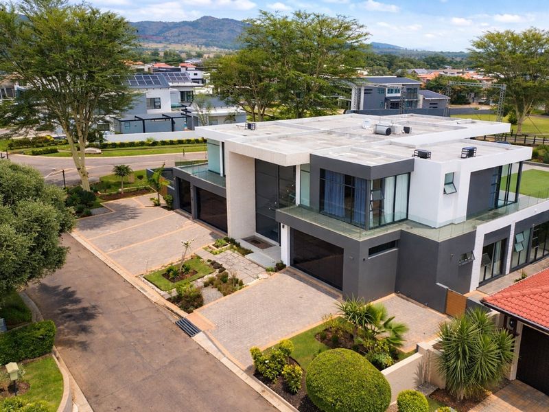 Aerial view of a modern, multi-level luxury residence featuring a paved driveway, integrated garage, glass balcony railings, and rooftop solar panels.