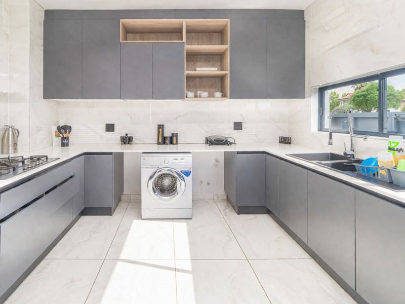 Modern kitchen featuring sleek grey cabinetry, marble-look wall and floor tiles, integrated gas hob, and a dedicated space for laundry appliances.