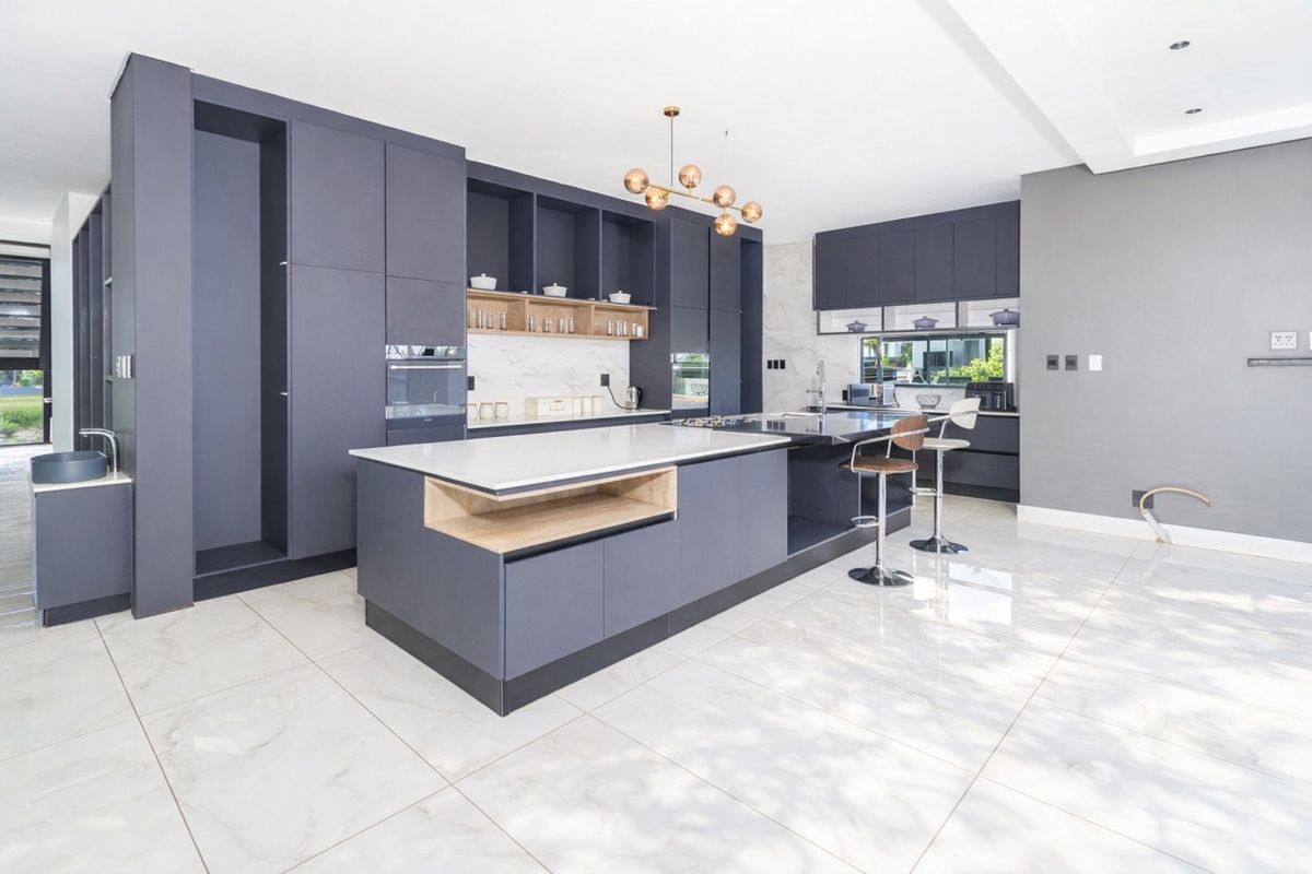 Modern kitchen featuring dark cabinetry, a large central island with stone countertops, integrated appliances, and polished marble-look floor tiles.