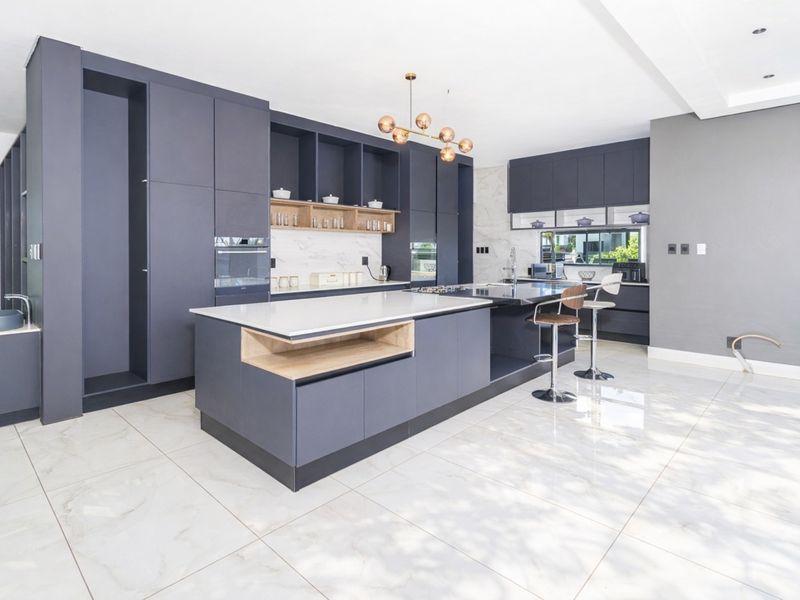 Modern kitchen featuring dark cabinetry, a large central island with stone countertops, integrated appliances, and polished marble-look floor tiles.