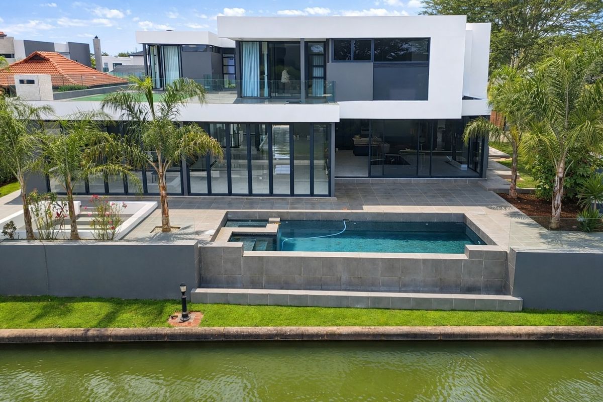 Modern waterfront residence featuring a sleek architectural design, expansive glass sliding doors, a tiled patio, and a private swimming pool overlooking the canal.