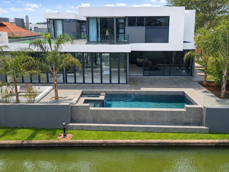 Modern waterfront residence featuring a sleek architectural design, expansive glass sliding doors, a tiled patio, and a private swimming pool overlooking the canal.
