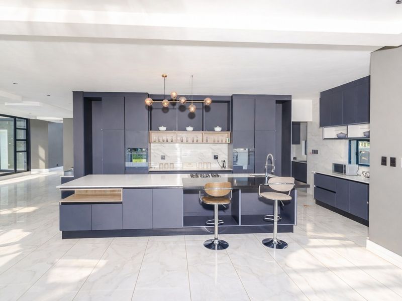 Modern open-plan kitchen featuring dark matte cabinetry, a large central island with stone countertops, integrated appliances, and polished marble-look floor tiles.