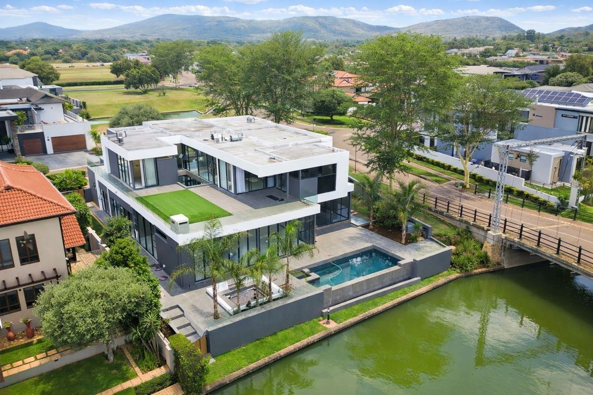 Aerial view of a modern multi-level luxury residence featuring a swimming pool, rooftop terrace, and direct waterfront access in a landscaped estate setting.