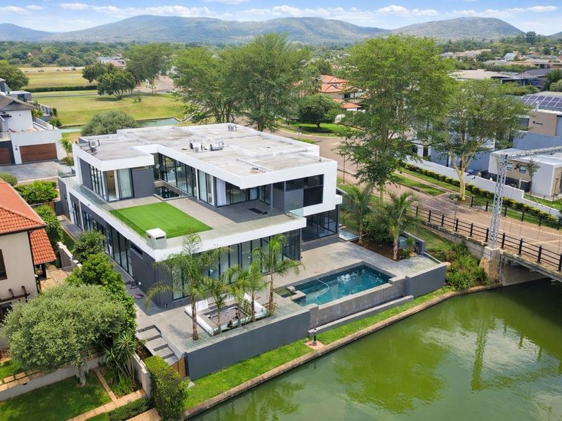 Aerial view of a modern multi-level luxury residence featuring a swimming pool, rooftop terrace, and direct waterfront access in a landscaped estate setting.