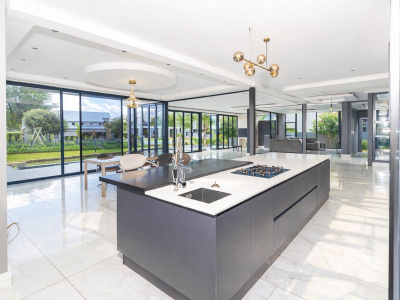 Spacious open-plan living area featuring a modern kitchen island with gas hob, stone countertops, and expansive floor-to-ceiling glass doors opening to the garden.