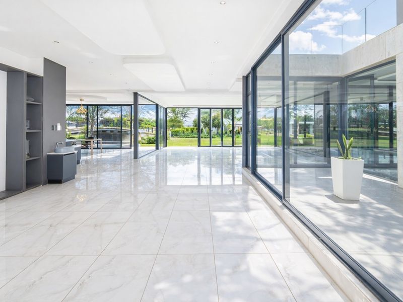 Spacious open-plan living area featuring large format porcelain tiles, extensive floor-to-ceiling glass walls, and modern built-in cabinetry with a sleek, minimalist design.