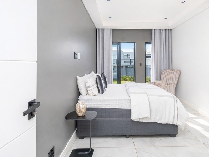 A modern, well-maintained bedroom featuring neutral grey accent walls, large format floor tiles, and sliding glass doors providing natural light and garden access.