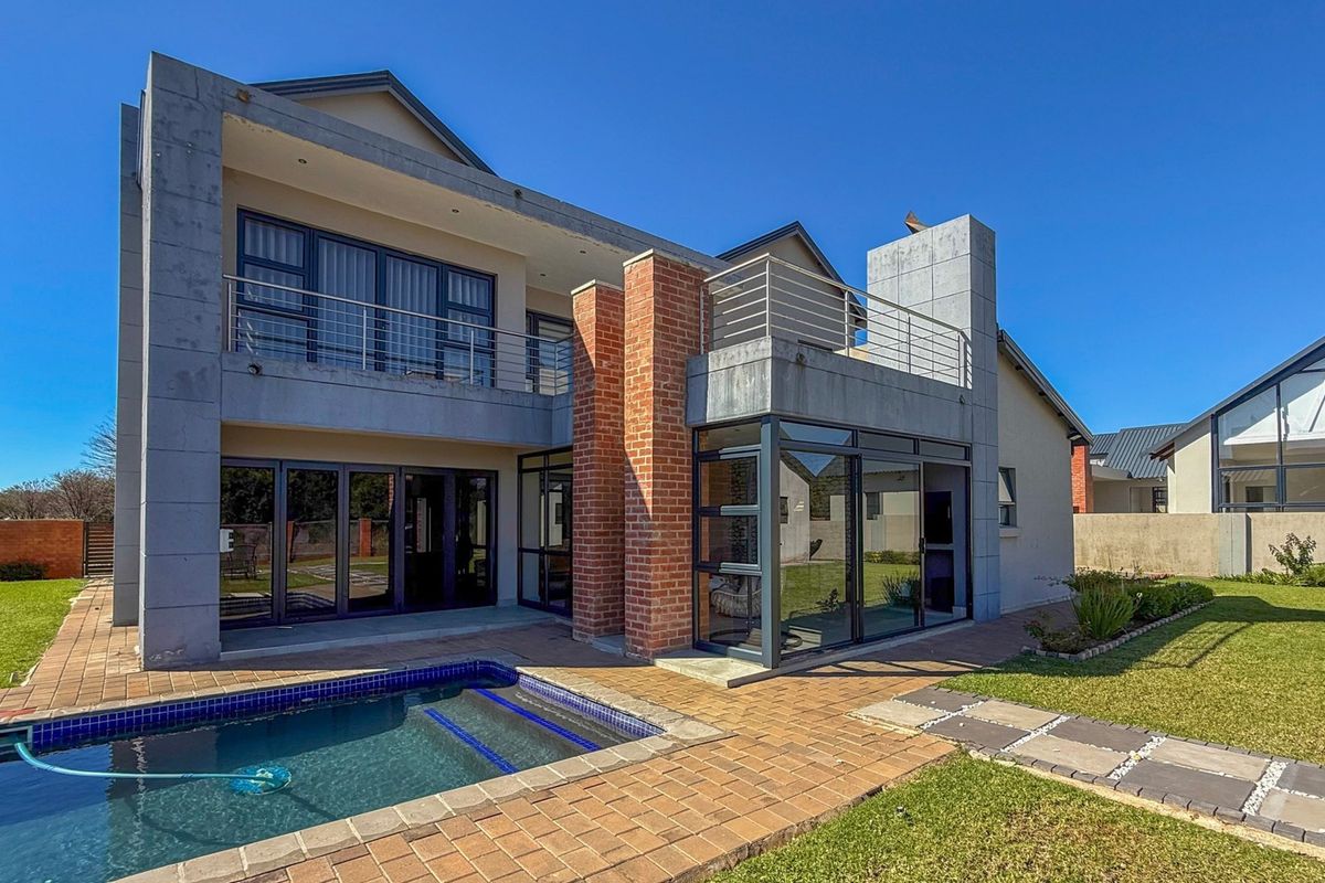 Rear view of a modern double-story house featuring a swimming pool, paved patio area, and an upper-level balcony with stainless steel railings.