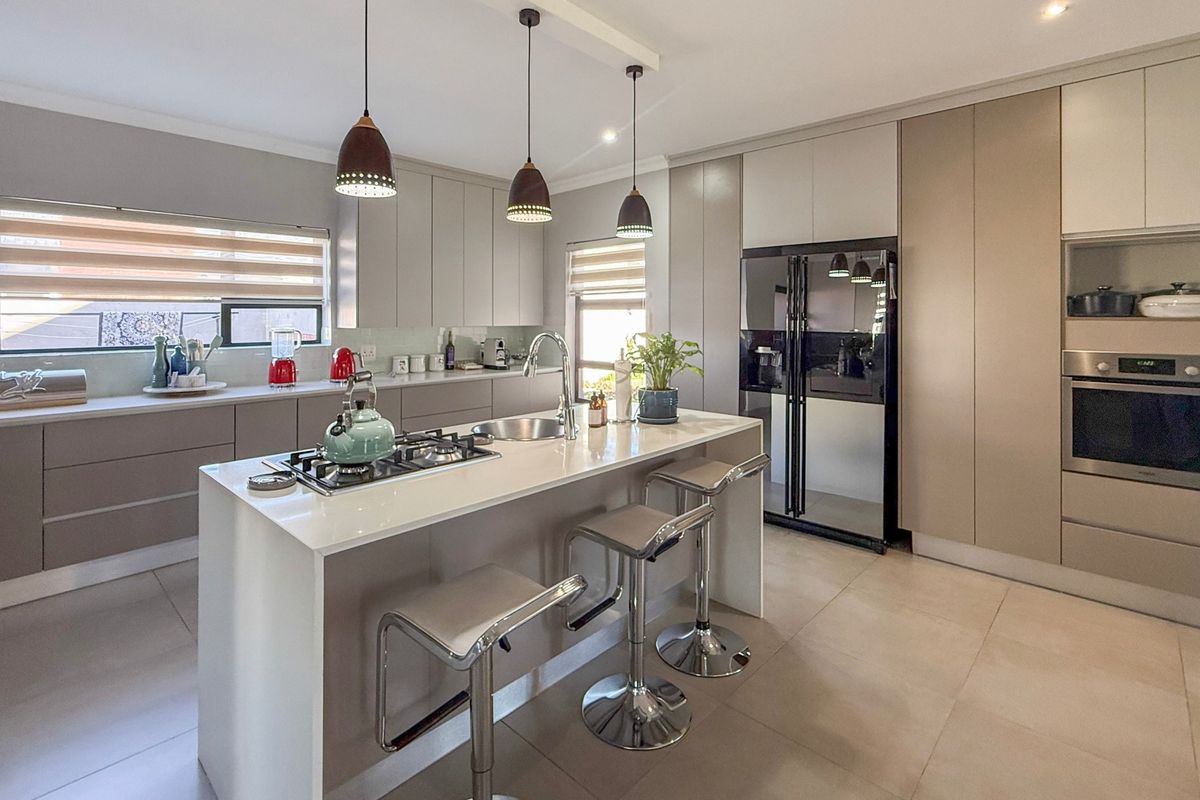 Modern kitchen featuring a central island with a gas hob, sleek integrated cabinetry, built-in oven, and high-quality tiled flooring.