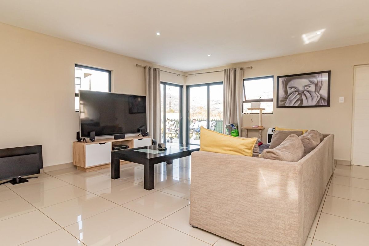A bright and spacious living room featuring large format floor tiles, recessed lighting, and sliding glass doors providing access to the outdoor area.
