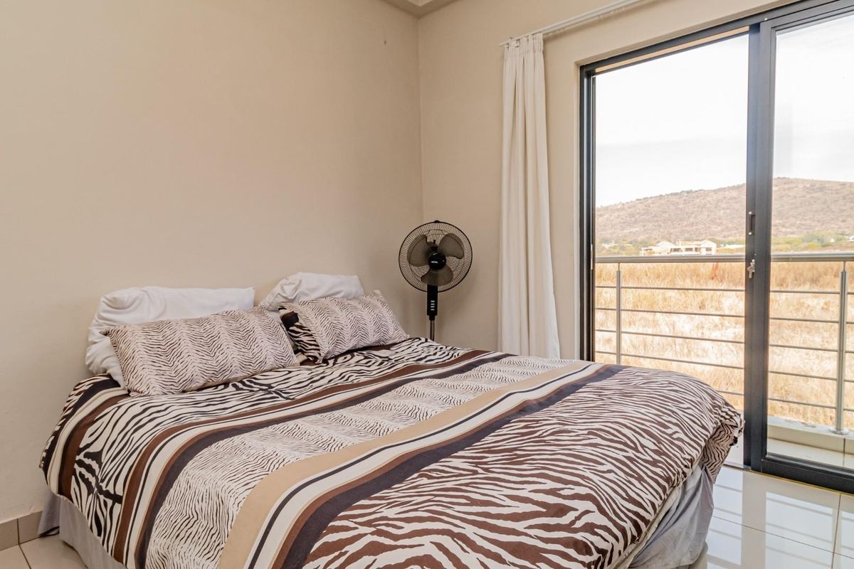 A bedroom featuring tiled flooring and a large sliding glass door that opens onto a balcony with scenic landscape views.