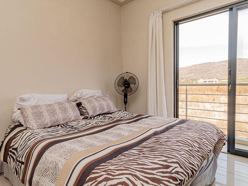 A bedroom featuring tiled flooring and a large sliding glass door that opens onto a balcony with scenic landscape views.