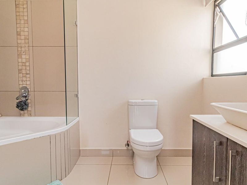 A modern bathroom featuring a built-in bathtub with a glass screen, a toilet, and a vanity cabinet with a vessel sink.