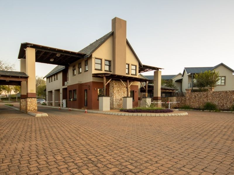 A well-maintained security entrance gatehouse featuring stone cladding, paved driveway, and boom gate access control for the residential estate.