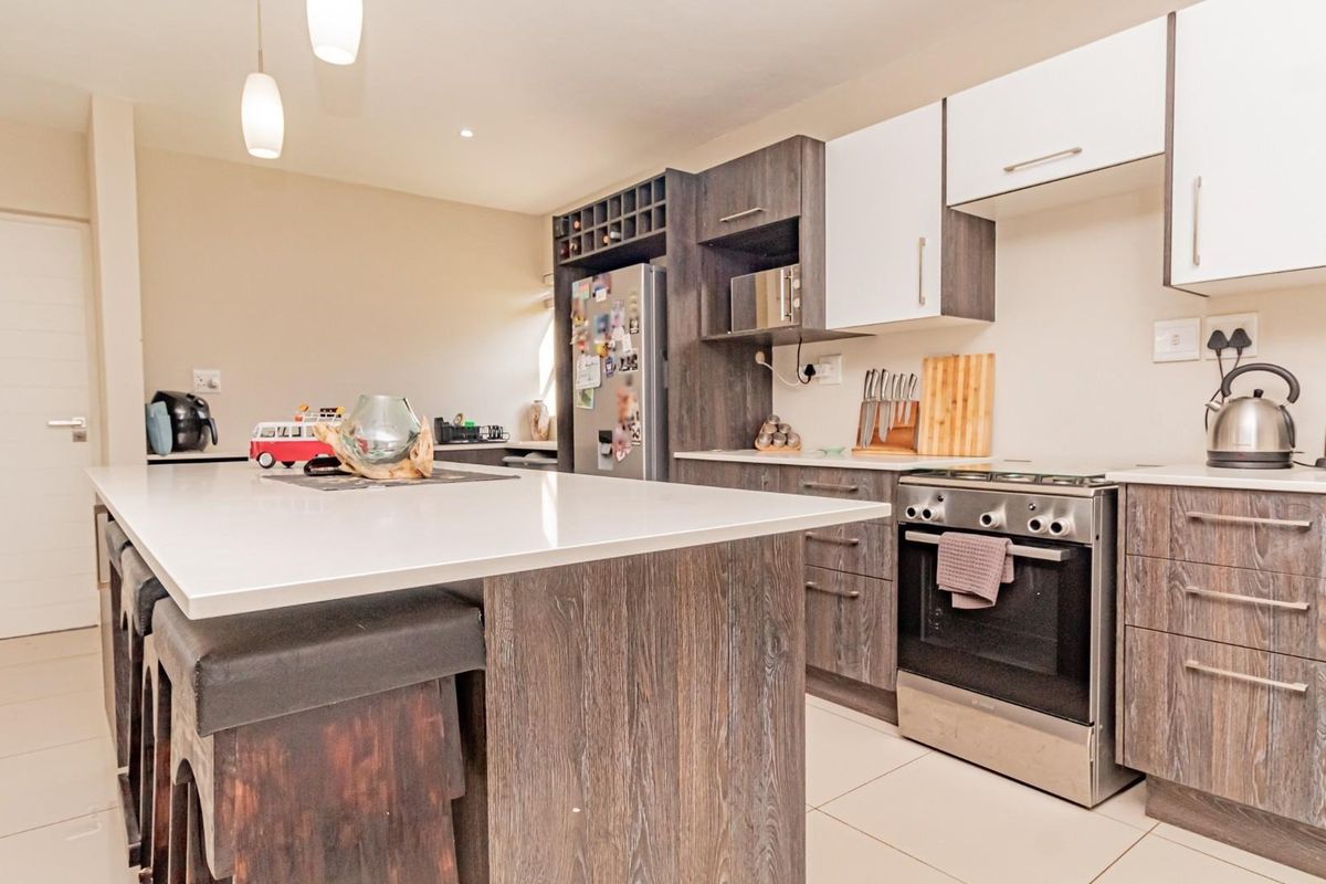 Modern kitchen featuring a central island with quartz countertops, dark wood-grain cabinetry, stainless steel oven, and tiled flooring.