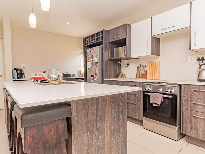 Modern kitchen featuring a central island with quartz countertops, dark wood-grain cabinetry, stainless steel oven, and tiled flooring.