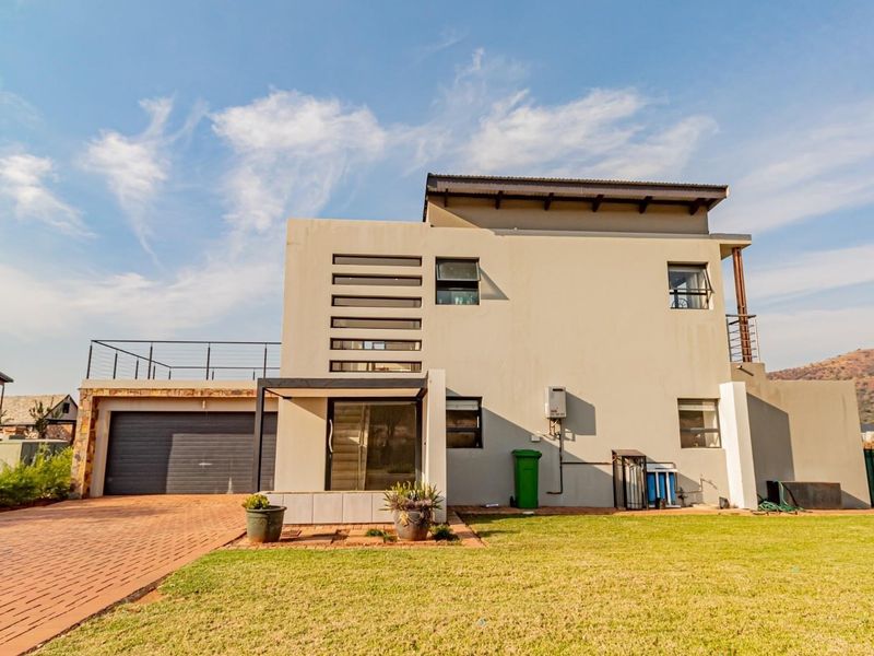 Rear view of a modern double-story house featuring a paved driveway, integrated garage, and an upper-level balcony with mountain views.