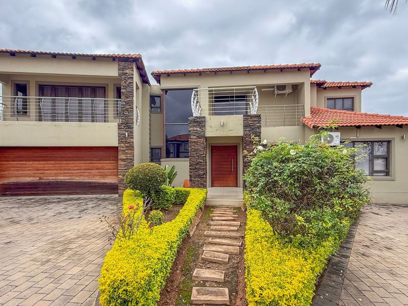 A well-maintained double-story residence featuring stone cladding, a tiled roof, a paved driveway, and a double garage with a wooden door.