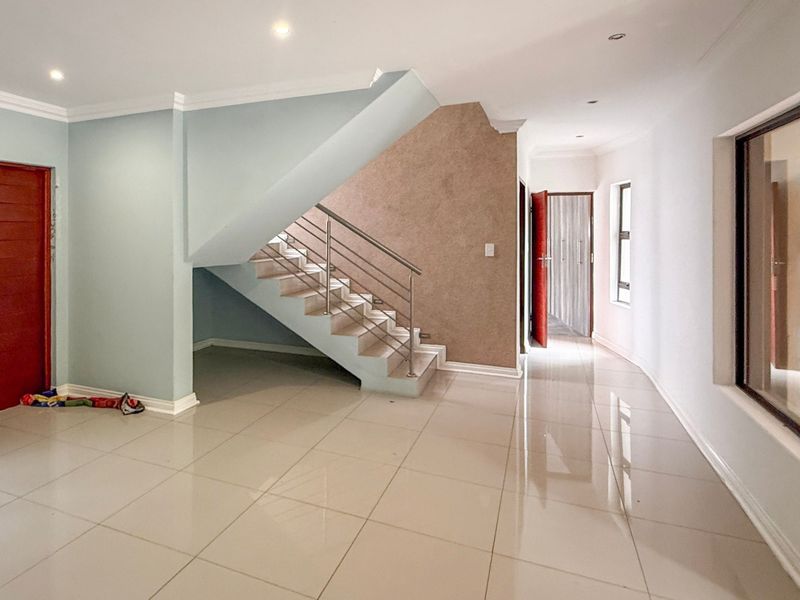 Spacious entrance hall featuring polished tiled flooring, a modern staircase with stainless steel balustrades, and a solid timber front door.
