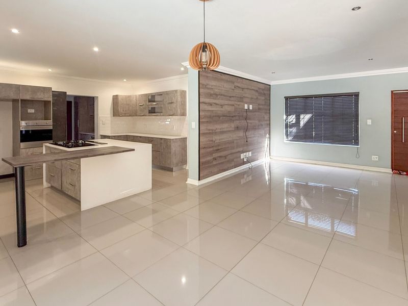 Spacious open-plan living and kitchen area featuring modern cabinetry, a central island with gas hob, built-in oven, and polished porcelain floor tiles.