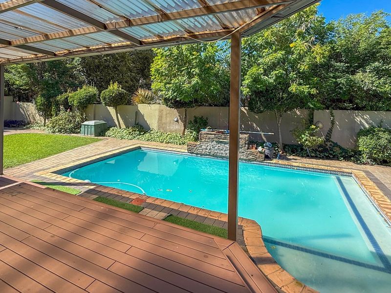 Outdoor entertainment area featuring a swimming pool, stone water feature, and a covered timber deck, set within a private garden with boundary walls.