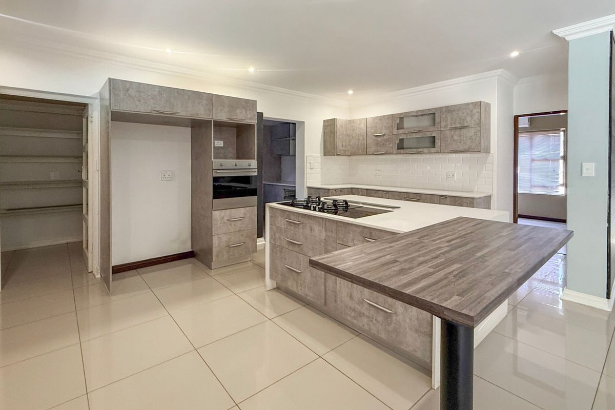 Modern kitchen featuring grey cabinetry, a central island with a gas hob, breakfast bar, subway tile backsplash, and an adjoining walk-in pantry.