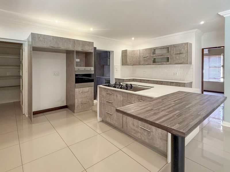 Modern kitchen featuring grey cabinetry, a central island with a gas hob, breakfast bar, subway tile backsplash, and an adjoining walk-in pantry.