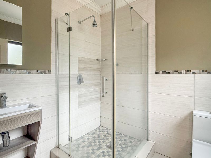 A modern, clean bathroom featuring a glass-enclosed shower, wall-mounted basin, and neutral tiled finishes throughout.