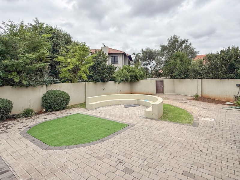 Rear garden area featuring a paved patio, curved built-in seating, and a section of artificial lawn, enclosed by a perimeter wall.