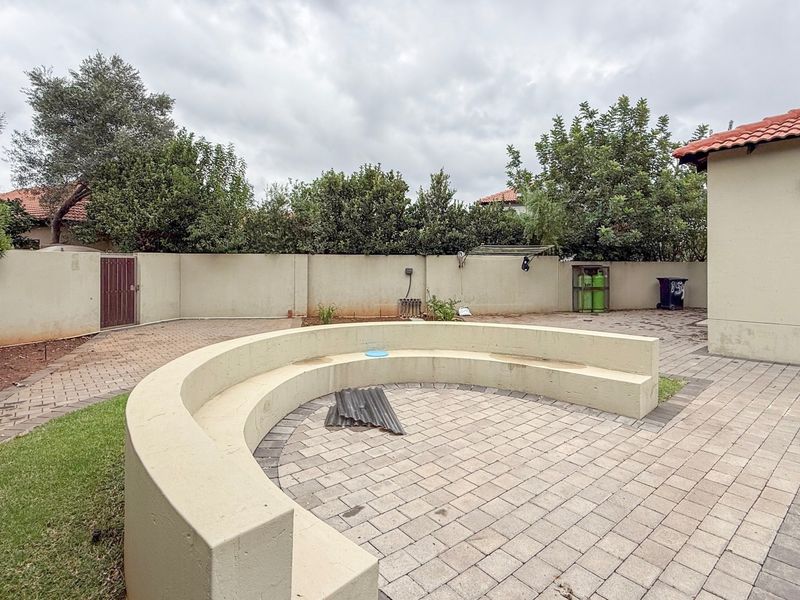 A rear courtyard area featuring a paved patio, a built-in curved concrete bench, and a perimeter boundary wall with established garden greenery.