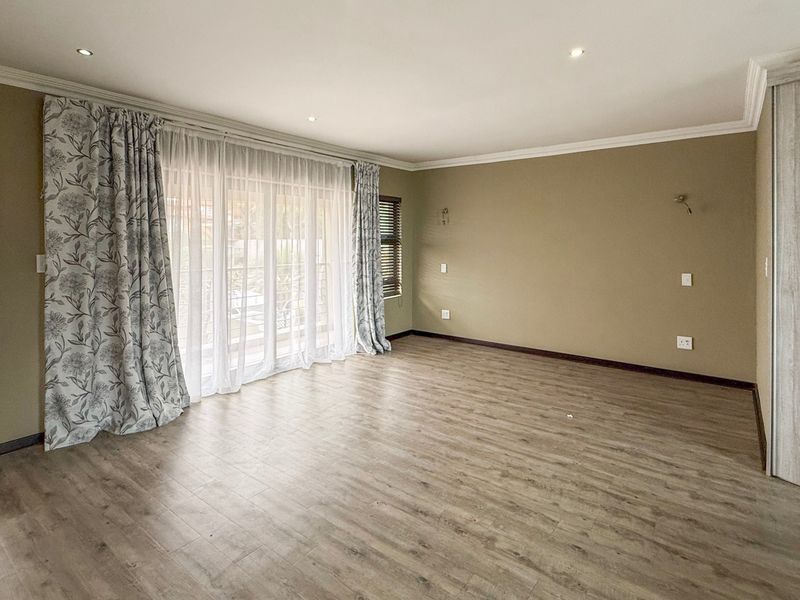 Spacious bedroom featuring light wood-look laminate flooring, built-in cupboards, recessed lighting, and a sliding glass door leading to an outdoor area.