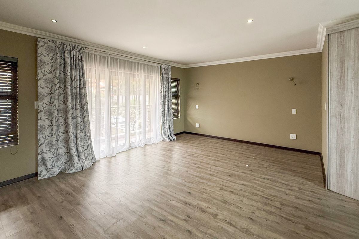 Spacious bedroom featuring light wood-look laminate flooring, built-in cupboards, recessed lighting, and a sliding glass door leading to an outdoor area.