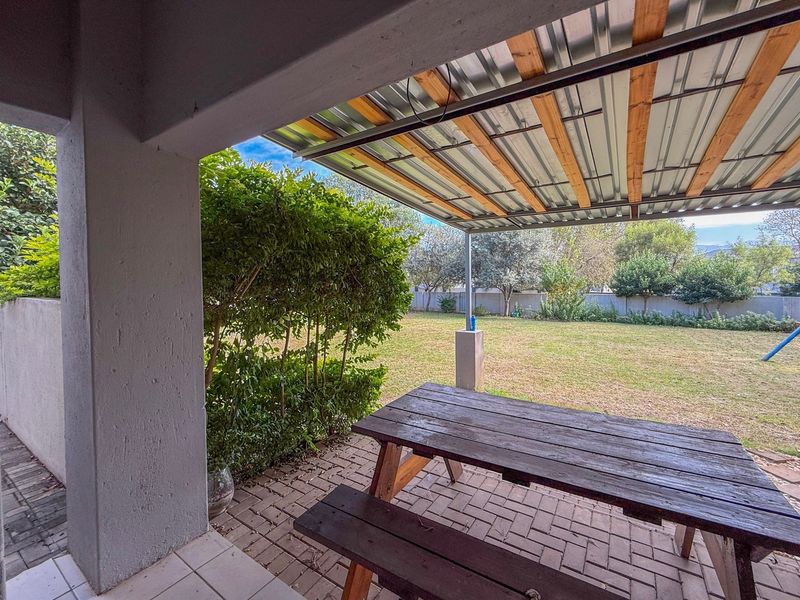 A covered outdoor patio area featuring a corrugated metal roof, paved flooring, and direct access to the rear garden.