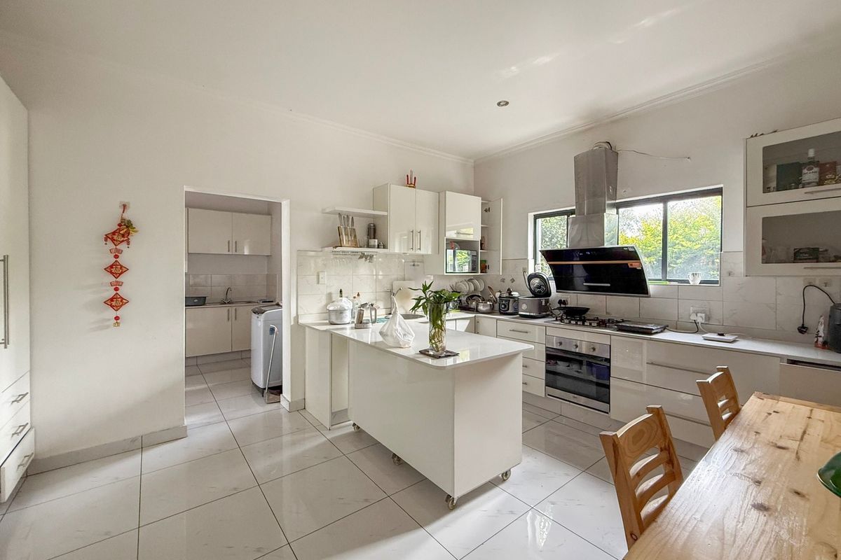 Modern white kitchen featuring a central island, built-in oven, gas hob, extractor fan, and tiled flooring, with an adjacent scullery area.