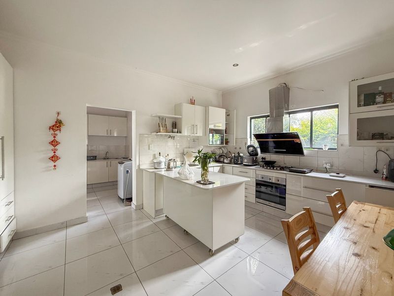 Modern white kitchen featuring a central island, built-in oven, gas hob, extractor fan, and tiled flooring, with an adjacent scullery area.