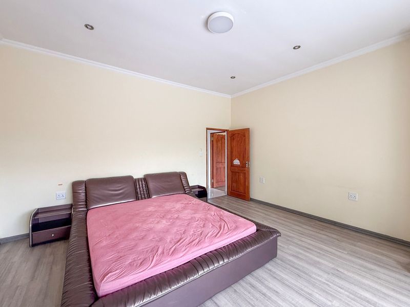 A spacious bedroom featuring light-toned laminate flooring, neutral walls, recessed ceiling lighting, and a solid timber door.
