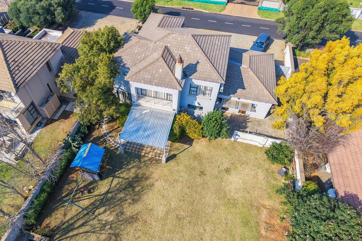 Aerial view of a residential property featuring a tiled roof, a covered patio area, and a spacious backyard with established trees.