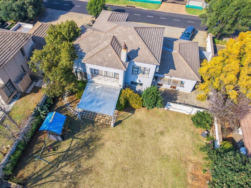 Aerial view of a residential property featuring a tiled roof, a covered patio area, and a spacious backyard with established trees.