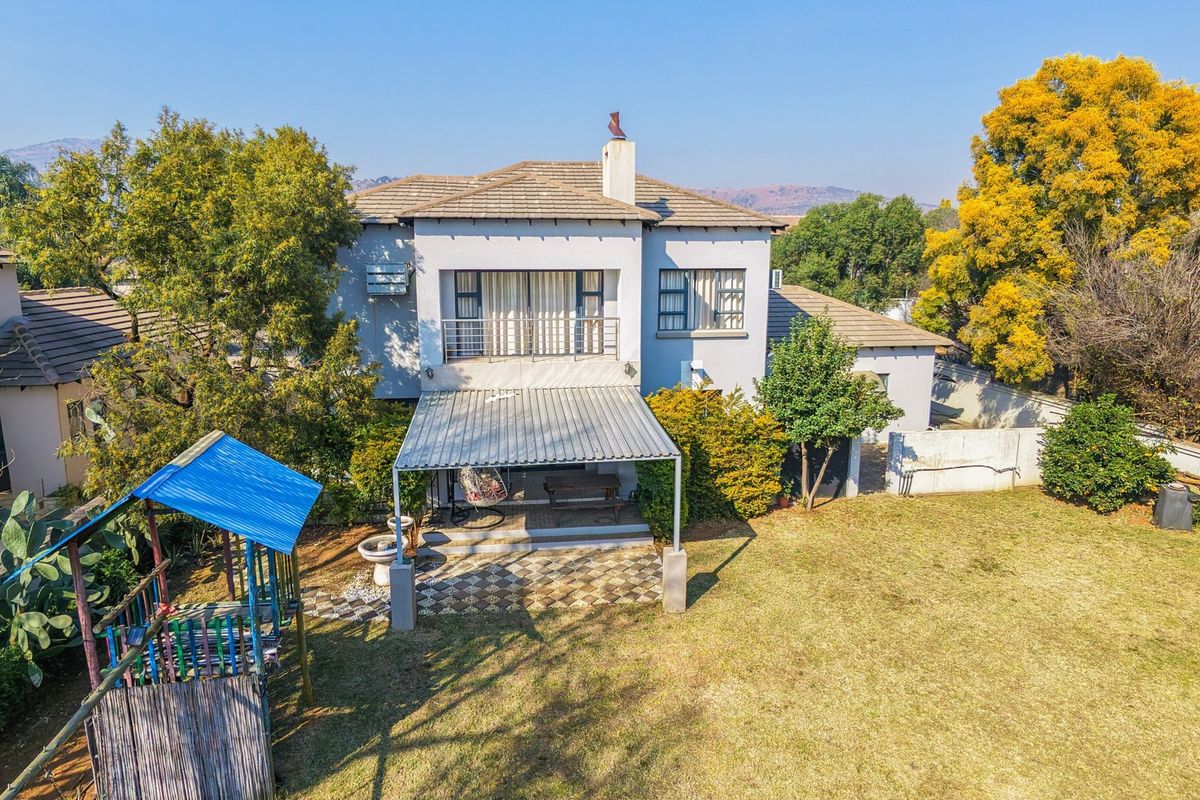 Rear view of the two-story house featuring a covered patio, upper-level balcony, tiled roof, and a spacious garden area.