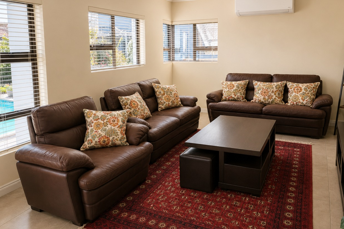 A well-maintained living room featuring tiled flooring, neutral wall tones, and a wall-mounted split-system air conditioner, with large windows providing natural light.