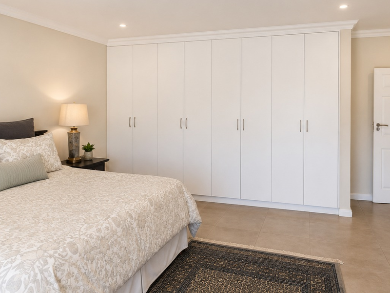 A well-maintained bedroom featuring extensive floor-to-ceiling built-in cupboards, neutral tiled flooring, and classic cornicing details.