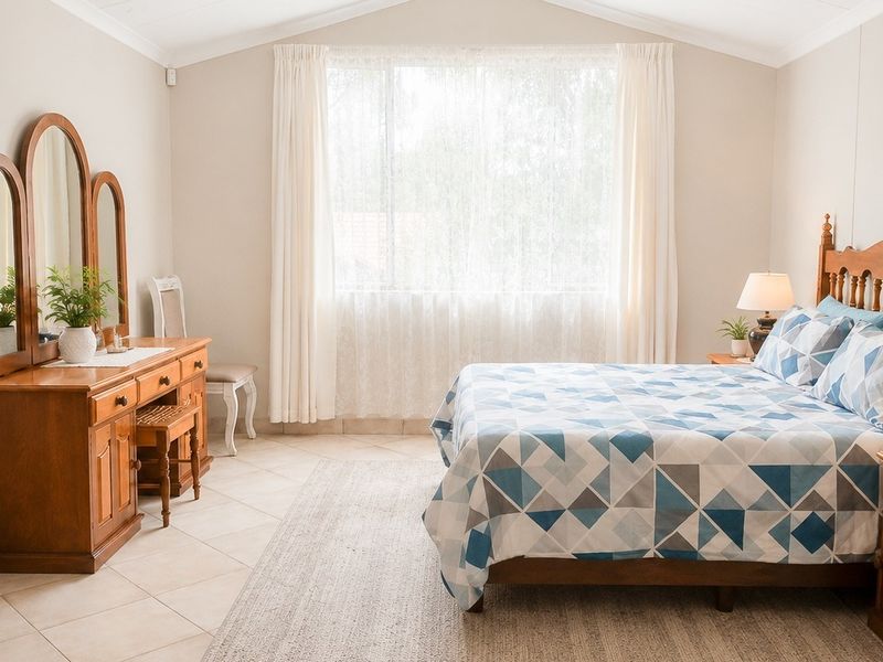 A well-maintained bedroom featuring tiled flooring, a vaulted ceiling, and a large window allowing for natural light.